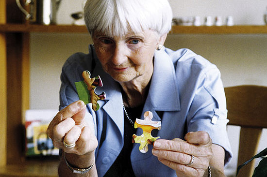 Eine Seniorin hält zwei Puzzlestücke in den Händen.