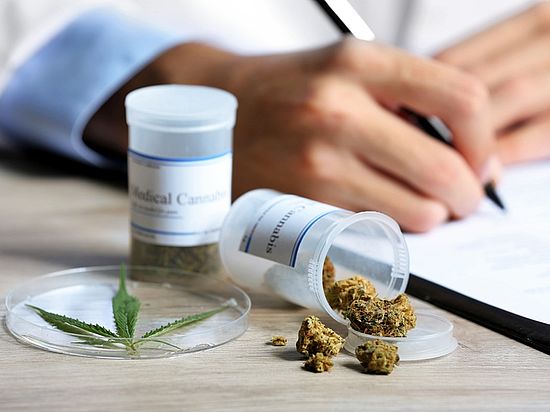 Ein Arzt schreibt ein Rezept für medizinisches Cannabis aus, das auf dem Tisch liegt.
