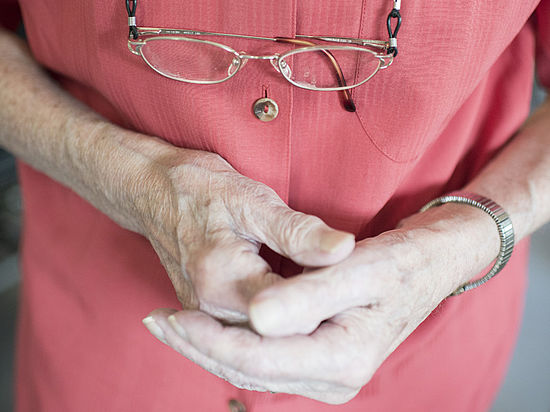 Ineinandergelegte Hände einer Seniorin und umgehängter Brille
