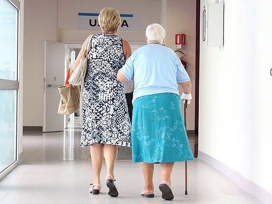 Ältere Frau wird auf dem Weg zu einem Arzttermin von einer jüngeren Frau begleitet.