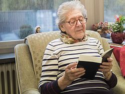 Seniorin sitzt in einem Sessel und ließt ein Buch.