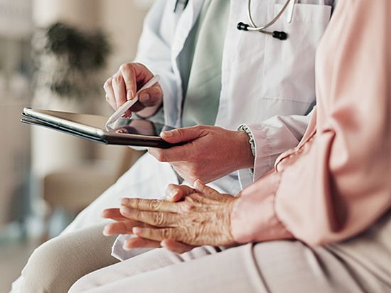 Ärztin zeigt einer älteren Patientin Informationen auf einem Tablet.