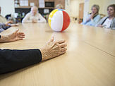 Seniorengruppe wirft sich am Tisch sitzend einen Ball zu
