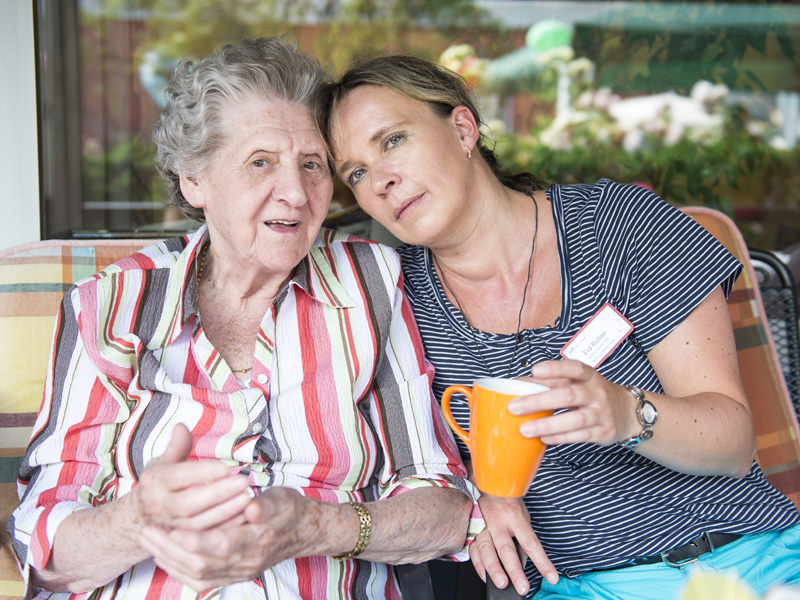 Seniorin und Pflegerin sitzen auf einer Terasse